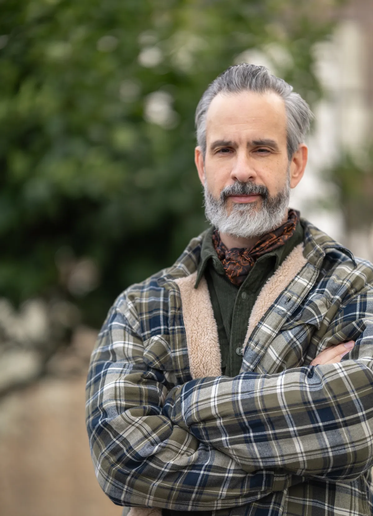 Wayne McRae standing outdoors with arms crossed, wearing a plaid shirt jacket.